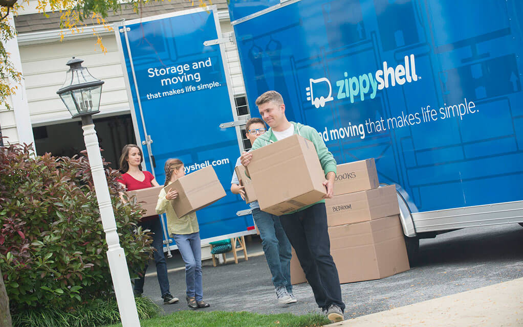 A suburban family unpacks boxes from their Zippy Shell container that has been delivered to their driveway
