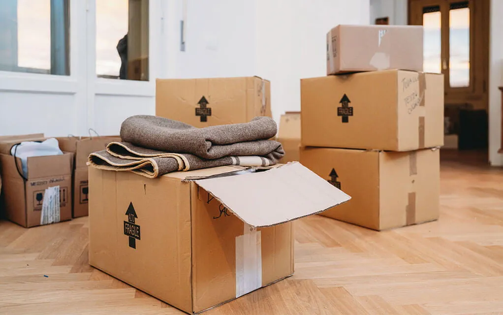 A pile of boxes, opened and unopened, sit on the floor of a home on a bright day ready to be loaded away