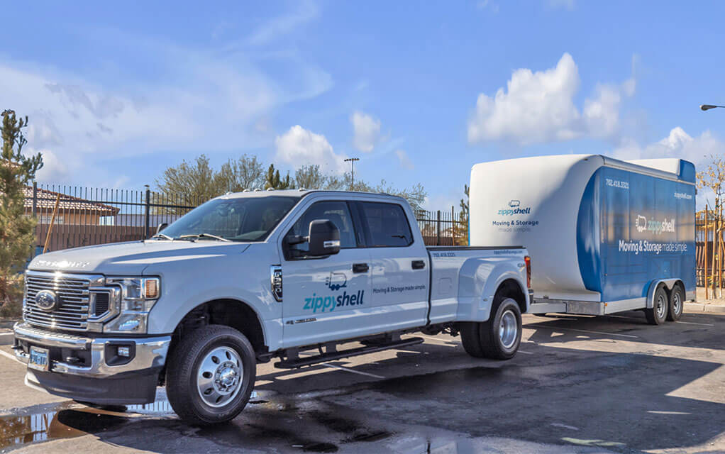 A recently cleaned white Zippy Shell delivery truck is about to transport a portable storage container to a customer
